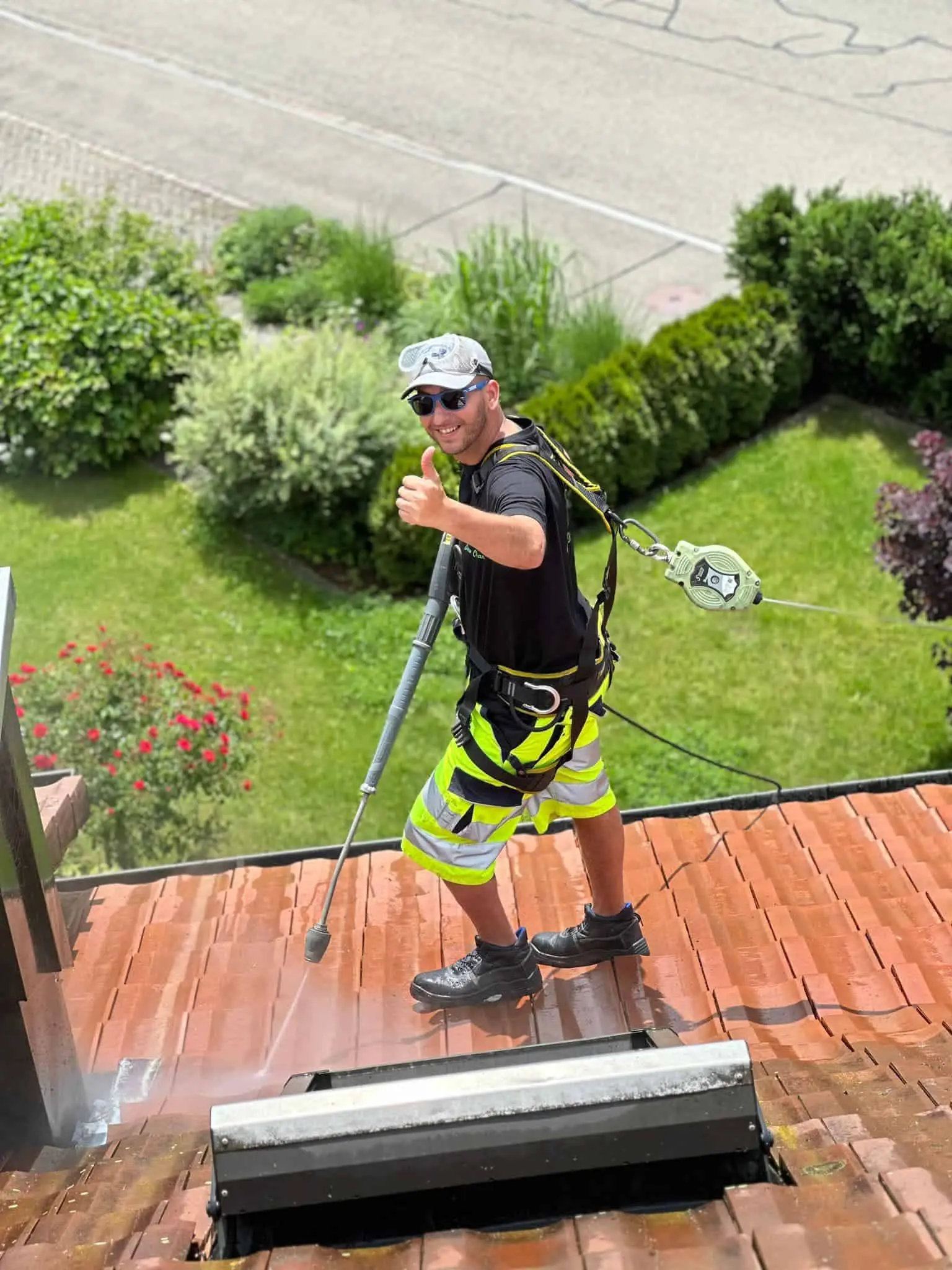 Mitarbeiter von Osmo Clean auf einem frisch gereinigten roten Ziegeldach, gesichert mit Auffanggurt und Höhensicherungsgerät